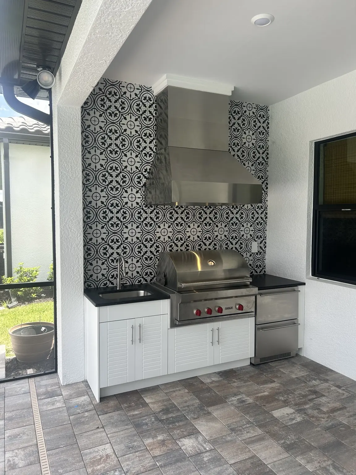 Outdoor kitchen with white WeatherStrong cabinets, stainless grill, hood and patterned tile