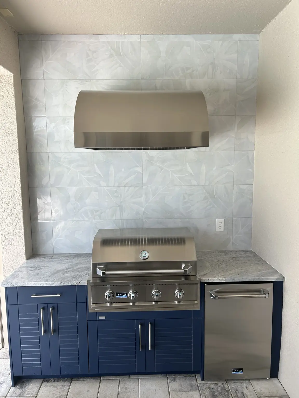 Compact outdoor kitchen with blue WeatherStrong cabinets, grill, refrigerator and wall tile